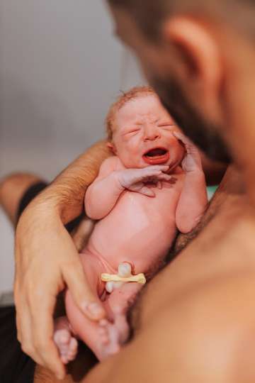 A newborn cries in his father's arms during an awe-inspiring moment in a cozy setting