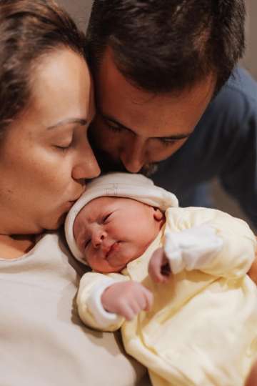 A loving couple fondly cuddles their newborn baby at home in a cozy setting during the evening hours